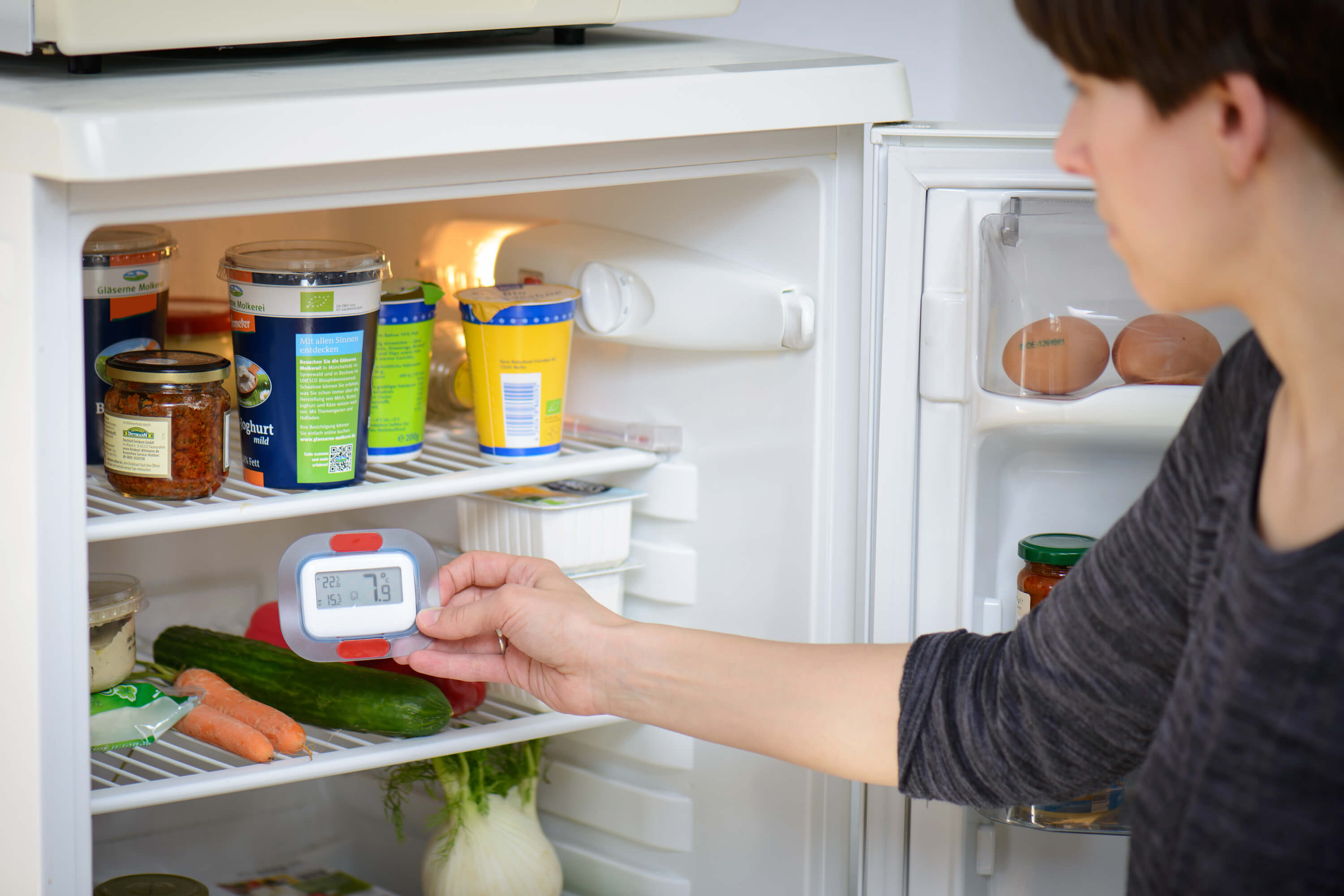 Frau misst die Innentemperatur im Kühlschrank mit einem Thermometer