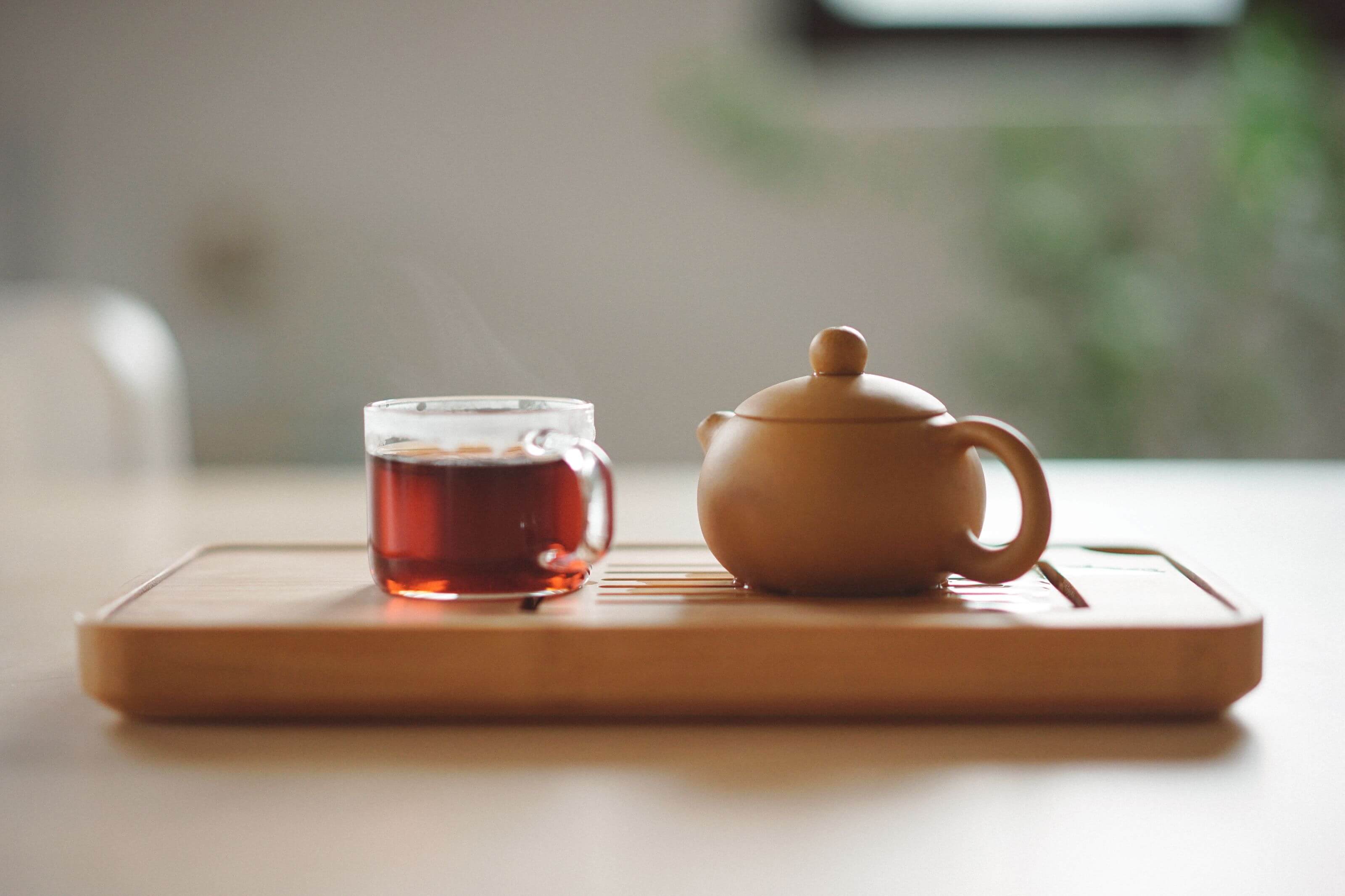 Teetasse und Kännchen auf Holztablett. Thema: Stromsparender Wasserkocher