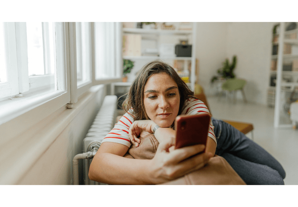 Eine Person liegt auf dem Sofa und schaut ins Handy. 