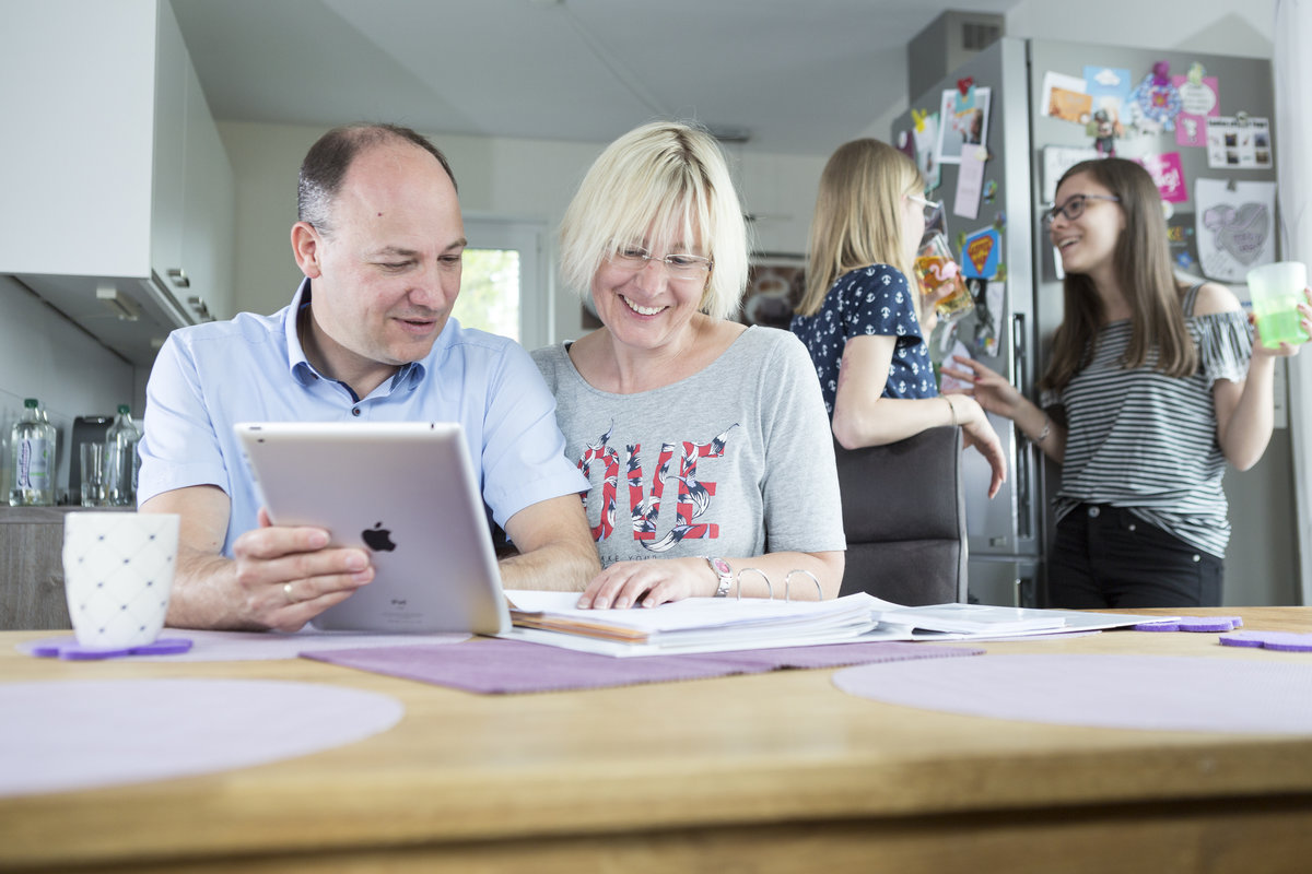 Zwei Personen sitzen am Küchentisch mit Tablet und Unterlagen. 