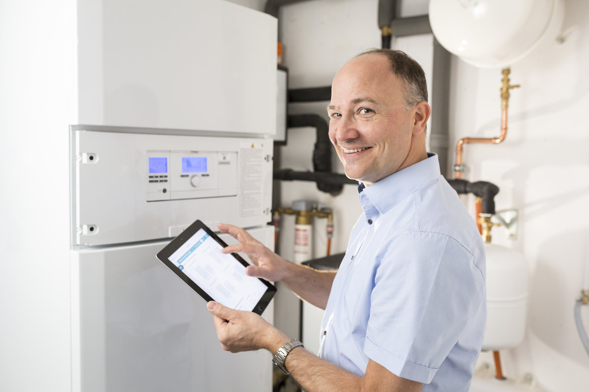 Eine Person steht mit einem Tablet in der Hand vor einer Wärmepumpe und kontrolliert ihre Funktion.