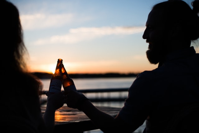 zwei Menschen stoßen bei Sonnenuntergang mit Bierflaschen an 