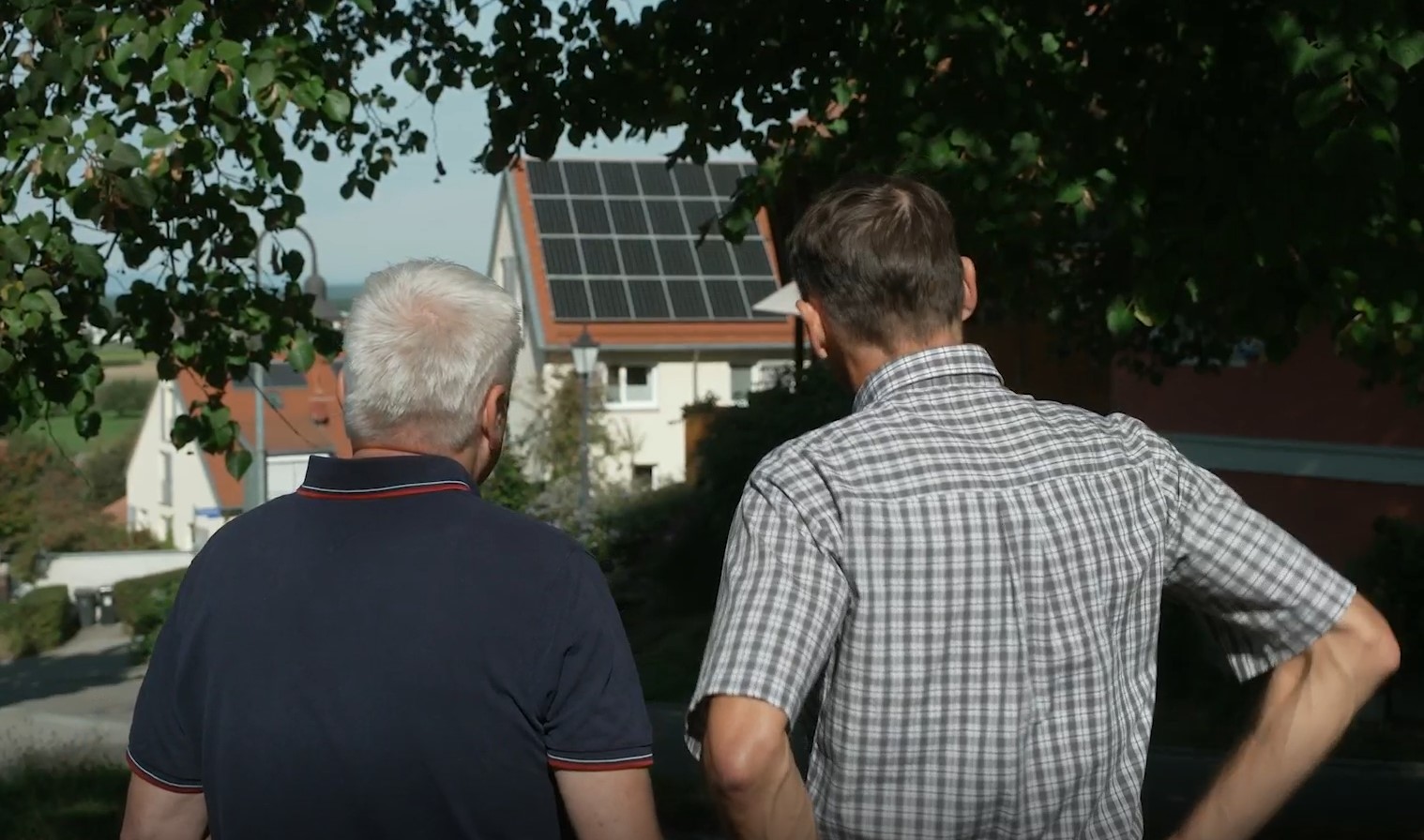 Zwei Männer betrachten ein Haus mit Photovoltaik aus der Ferne