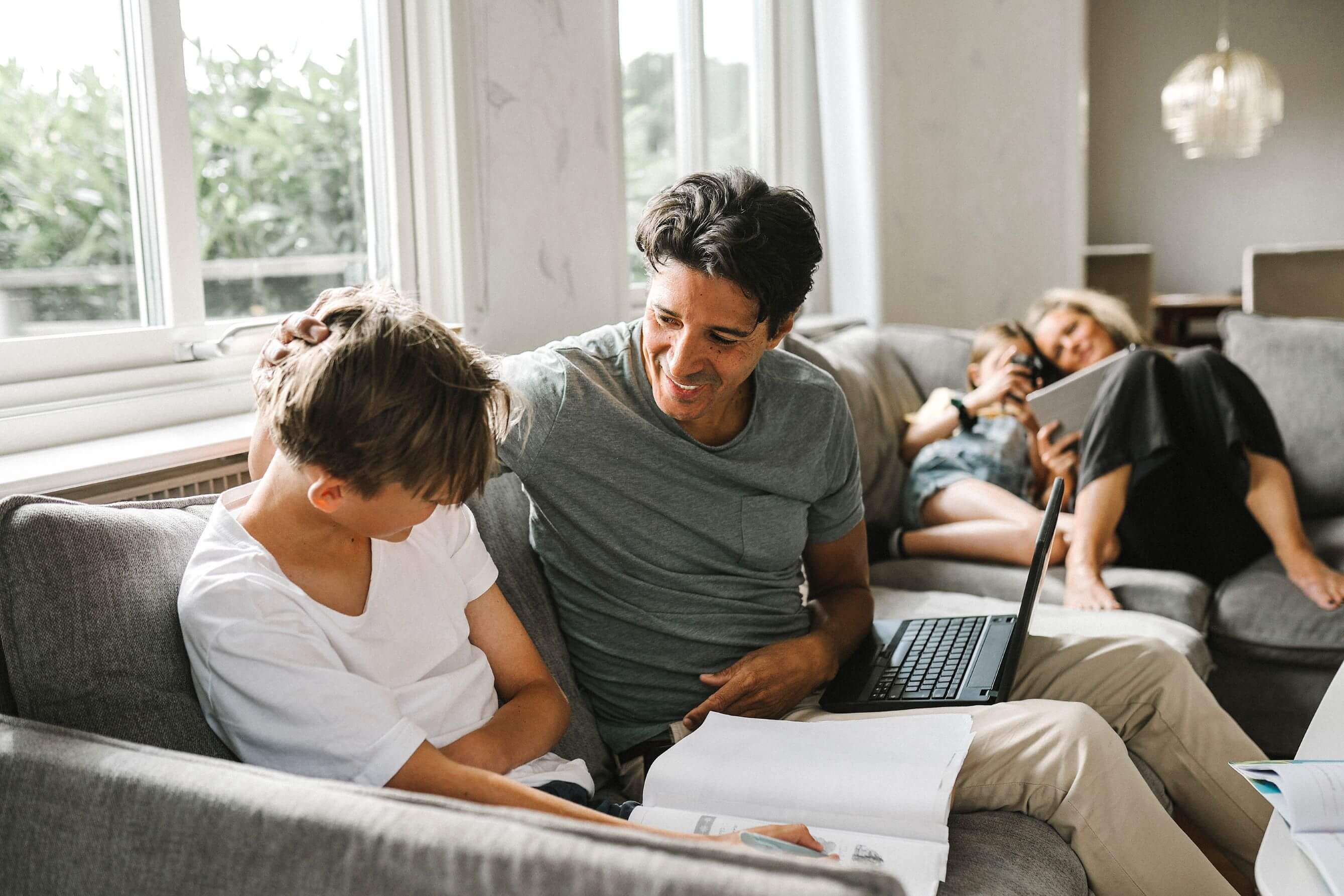 Vater und Sohne sitzen auf grauem Sofa, im Hintergrund Mutter und Tochter.