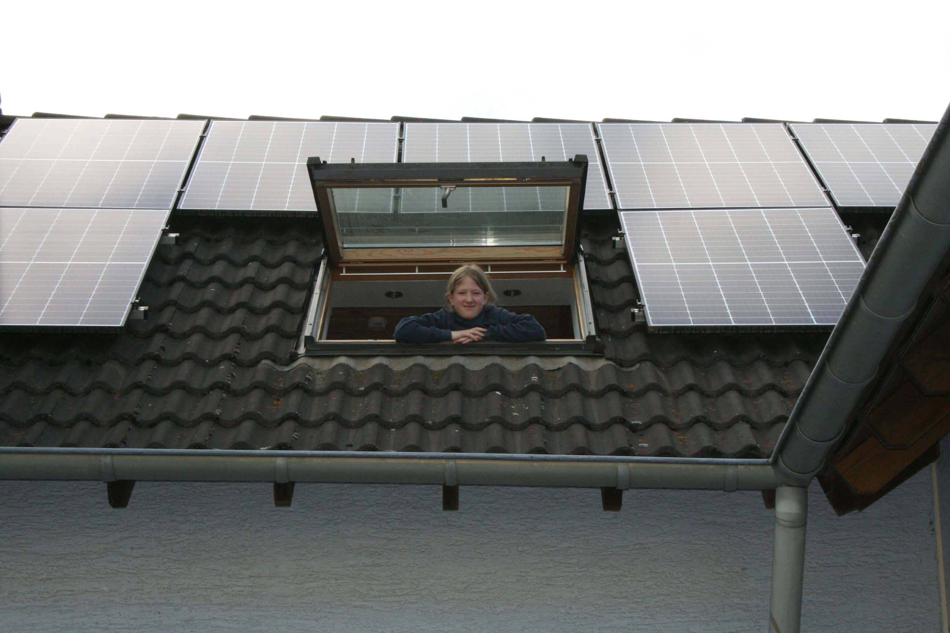 Mädchen schaut aus Dachfenster, drum herum PV-Module